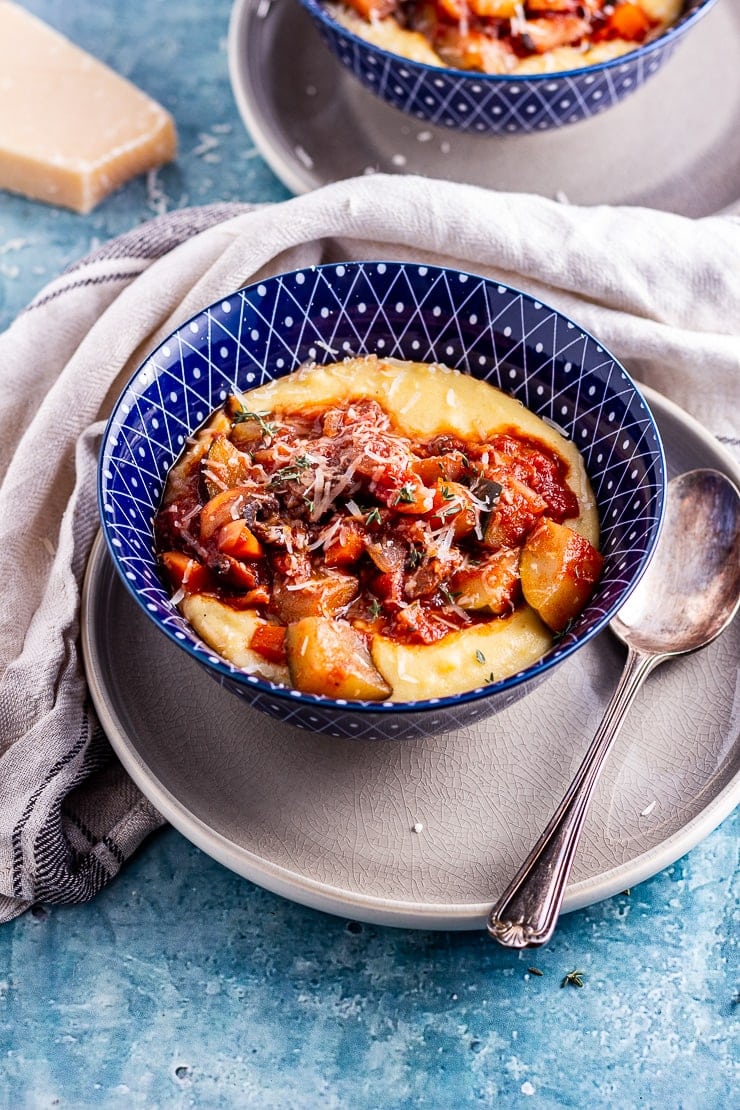 Side angle shot of vegetable stew on creamy polenta in a blue bowl