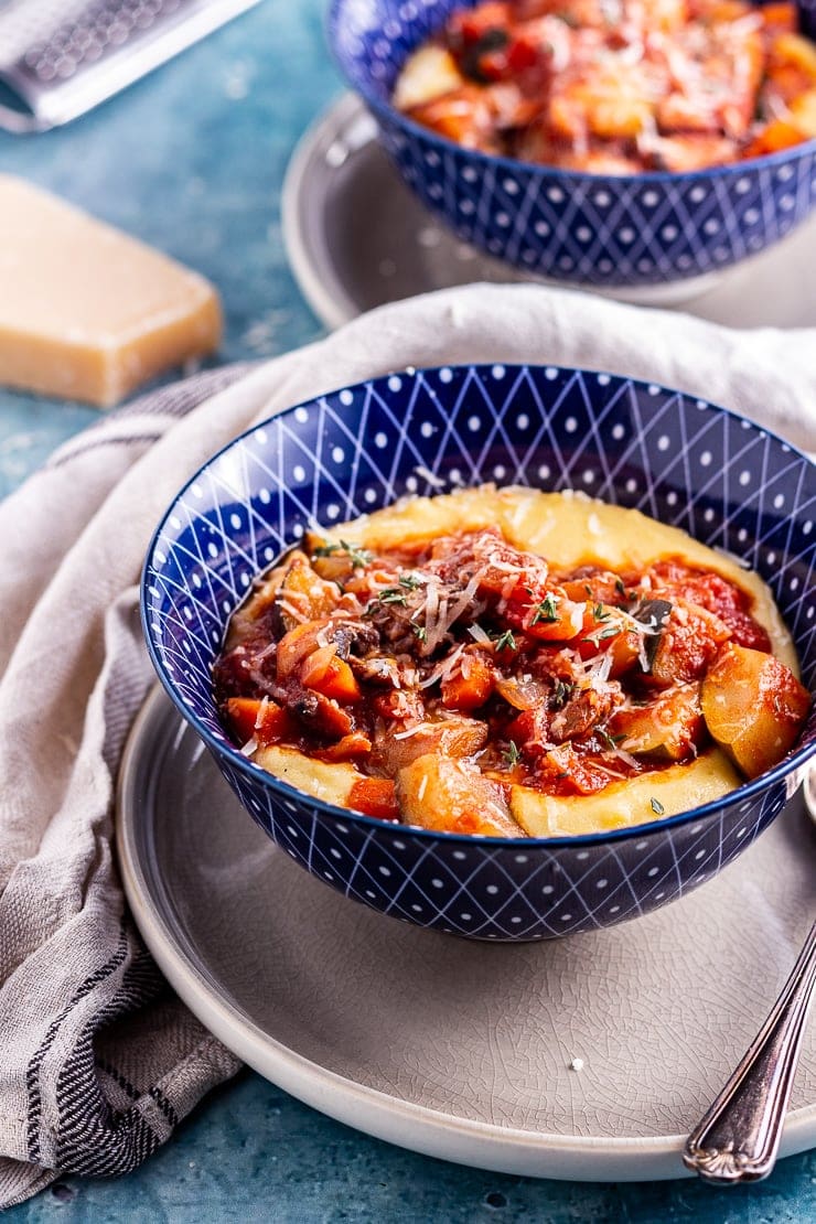 Side angle shot of vegetable stew with creamy polenta in a blue bowl with a spoon and cloth