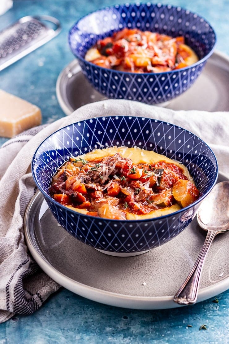 Side on shot of vegetable stew with creamy polenta in a blue bowl with a spoon and cloth