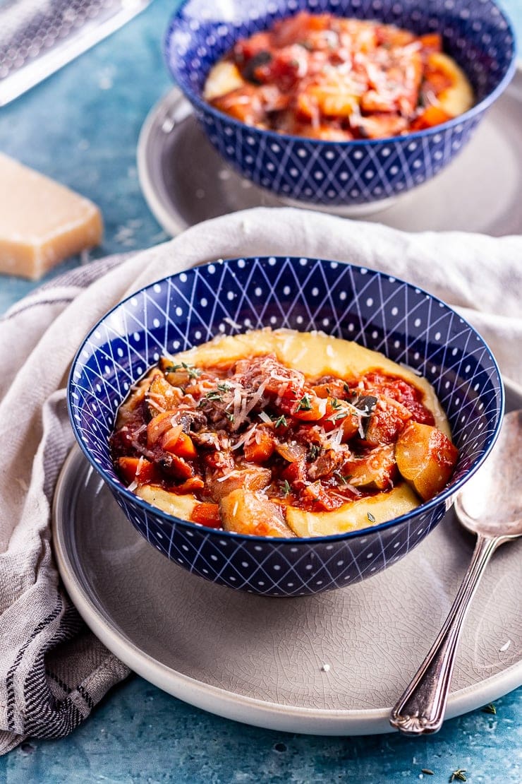 Side on shot of vegetable stew with creamy polenta in a blue bowl on a plate