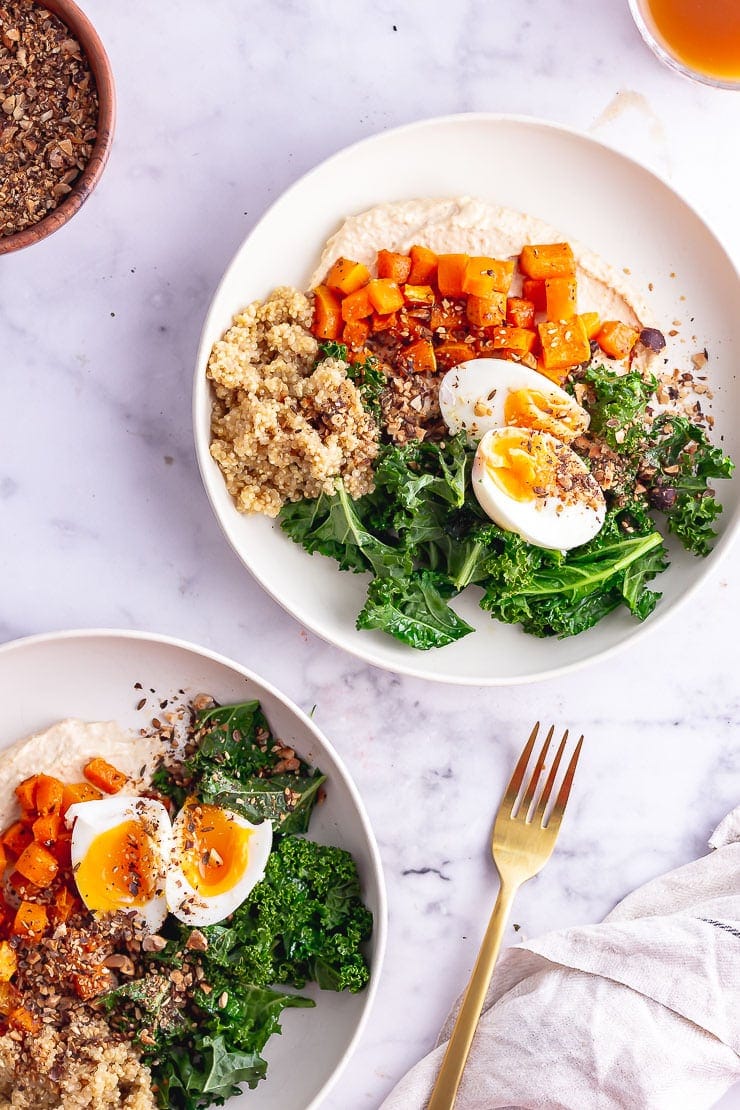 Overhead shot of vegetarian breakfast bowls with a gold fork on a marble background