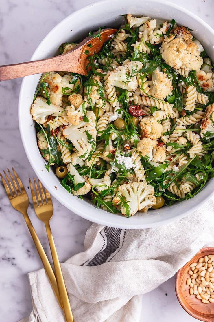 Overhead shot of roasted cauliflower pasta with gold forks and a wooden bowl of nuts