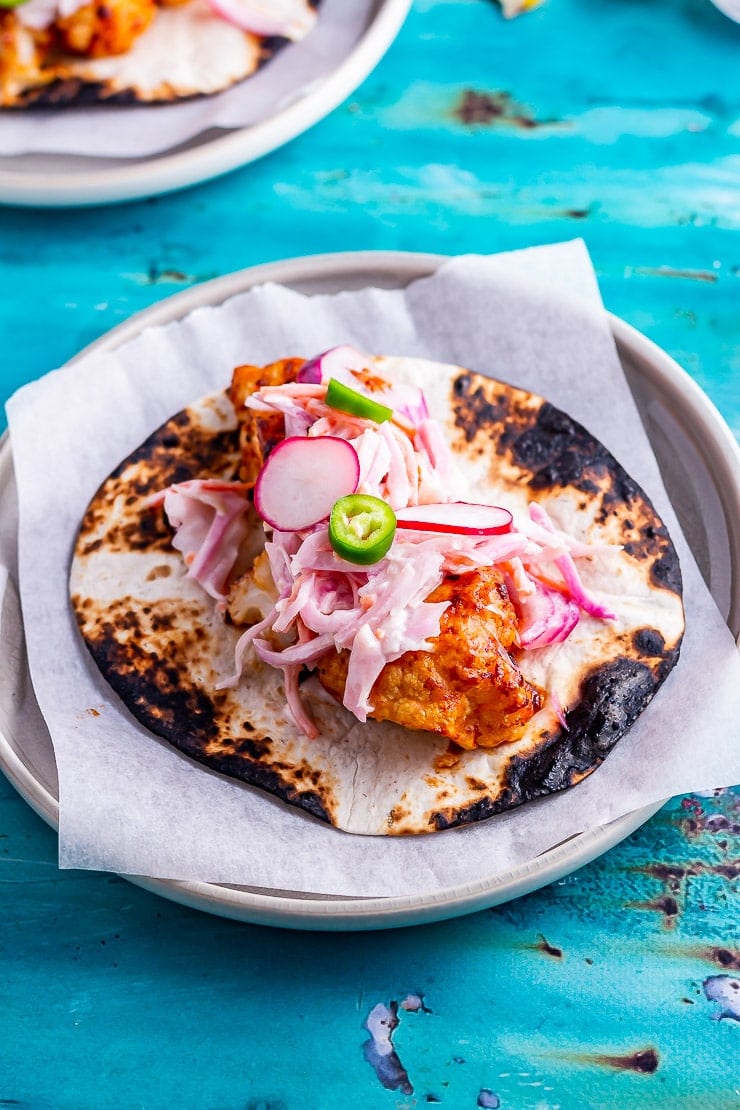 Side on shot of cauliflower tacos on a plate on a blue background