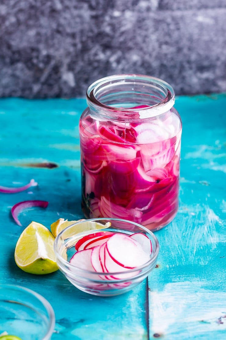 Jar of quick pickled red onions for cauliflower tacos on a blue background with radish and limes
