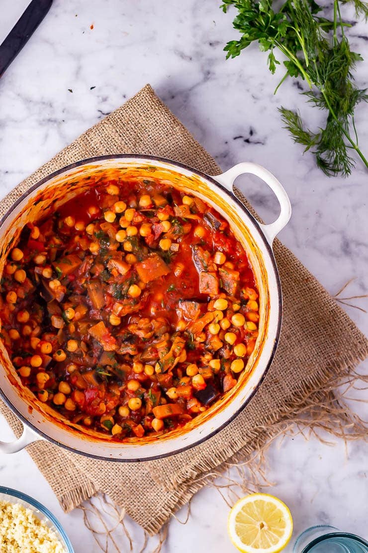 Overhead shot of harissa chickpea stew on a woven mat over a marble background with herbs and lemon