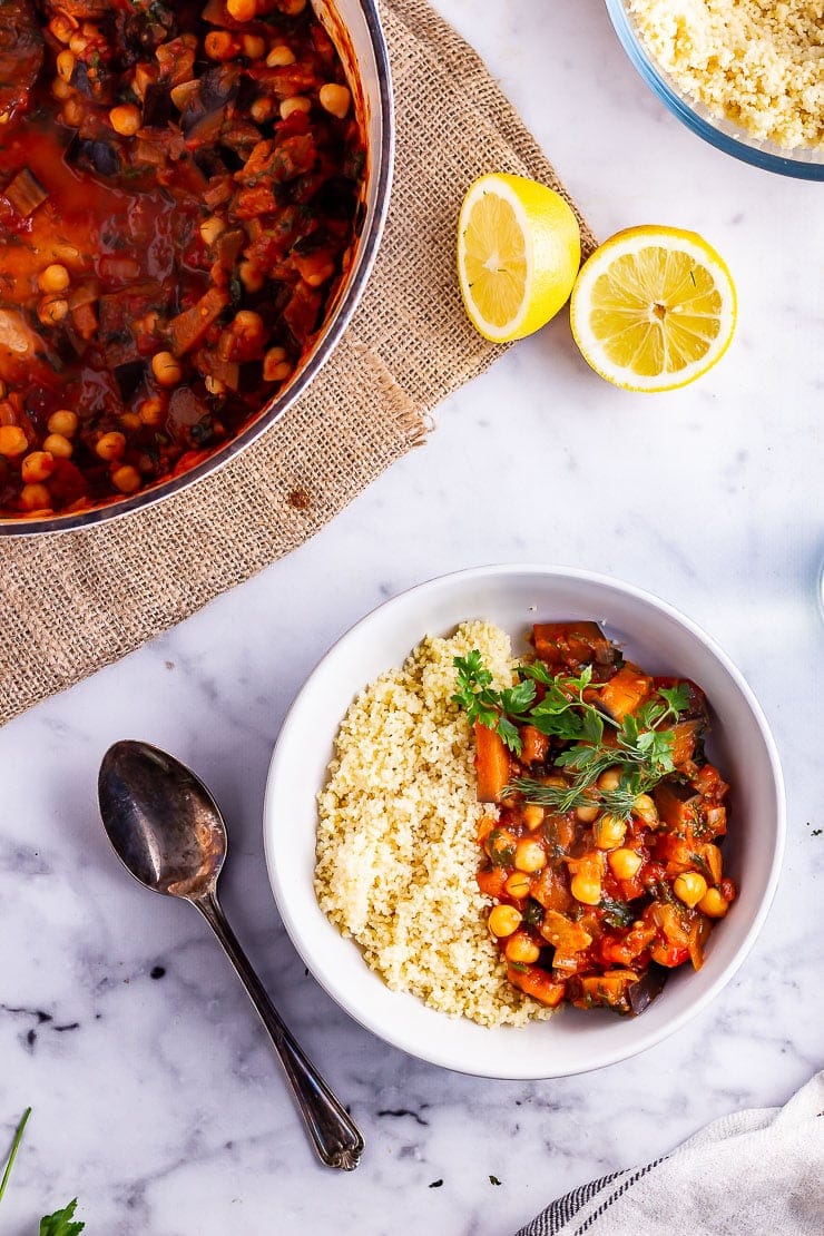 Overhead shot of harissa chickpea stew with couscous in a bowl on a marble background with lemon