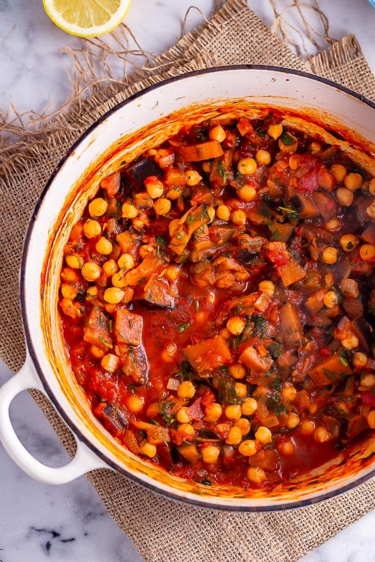 Overhead shot of harissa chickpea stew in a white pot on a woven mat