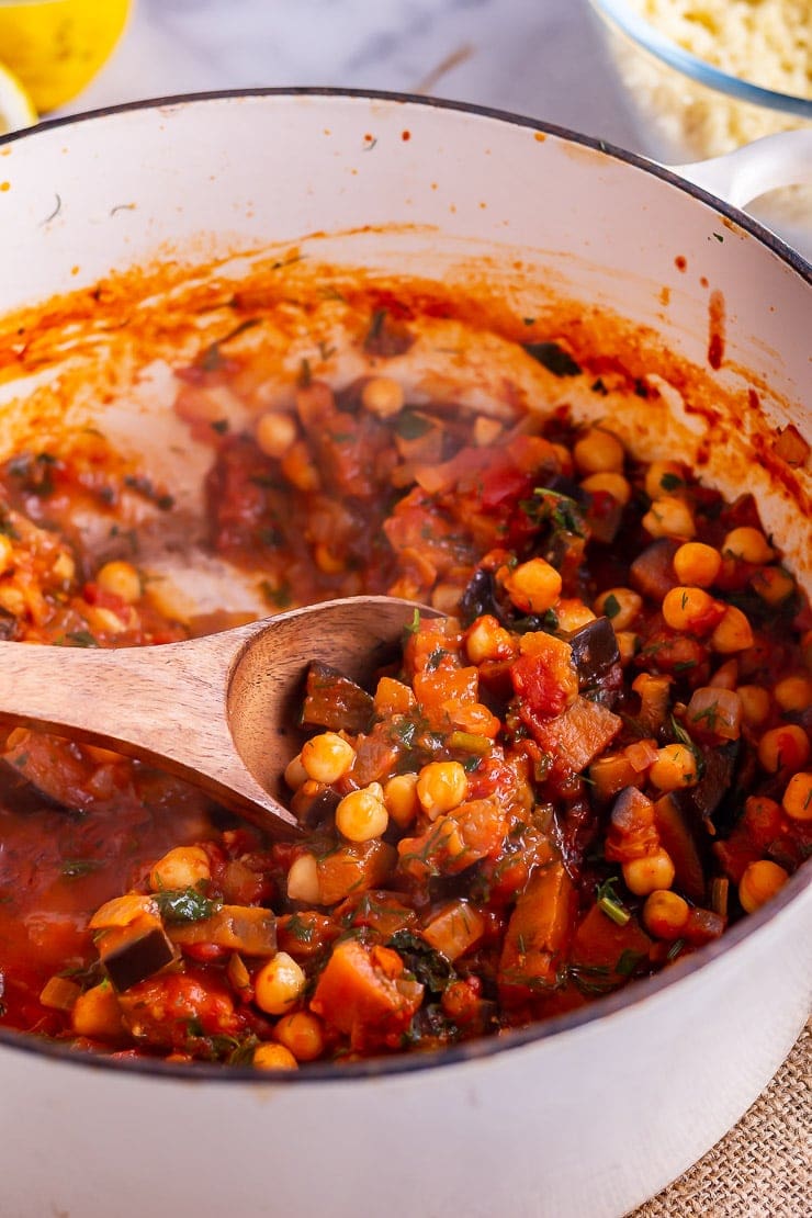 Side on shot of harissa chickpea stew with a wooden spoon in a white pot