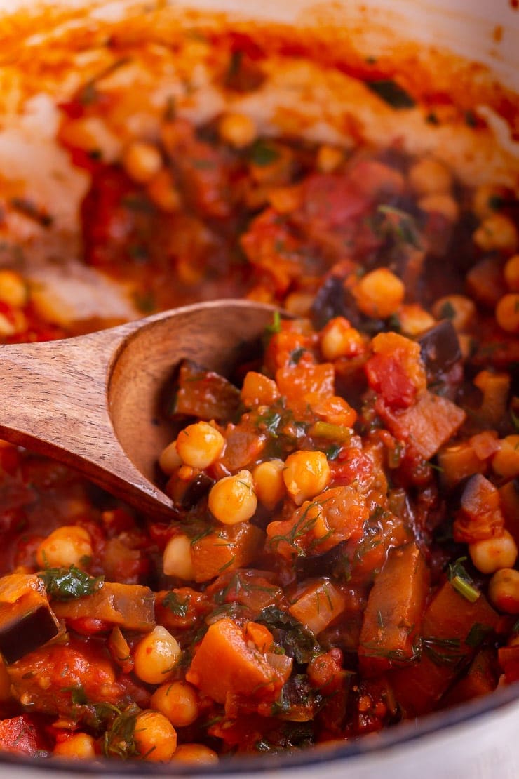 Close up of harissa chickpea stew with a wooden spoon in the pot