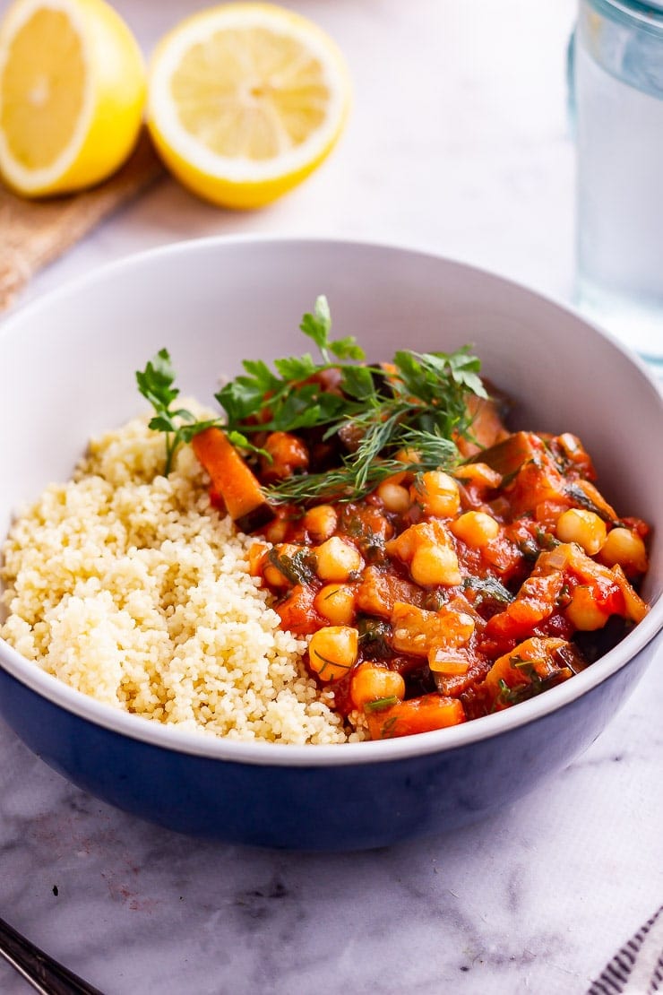 Side on shot of harissa chickpea stew with couscous and herbs in a blue bowl