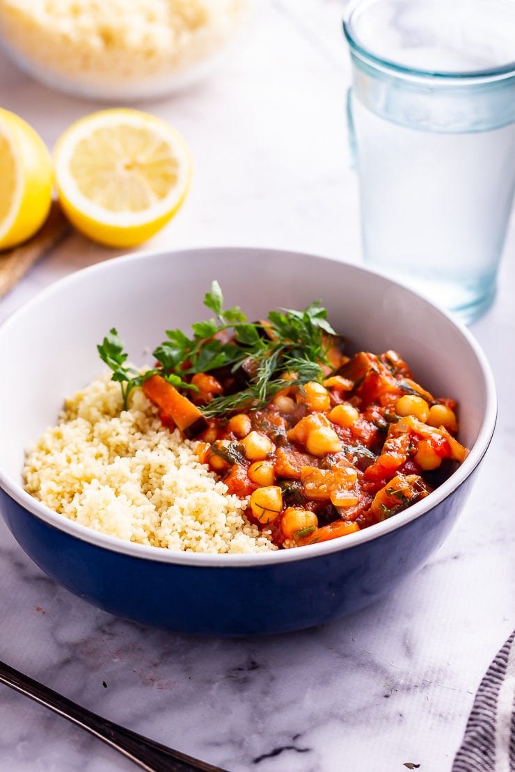 Side on shot of harissa chickpea stew with couscous in a blue bowl on a marble background