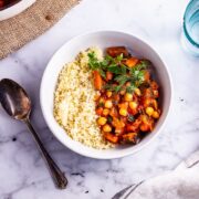 Overhead shot of harissa chickpea stew with couscous on a marble background with a spoon and lemon