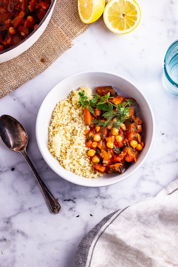 Overhead shot of harissa chickpea stew with couscous on a marble background with a spoon and lemon