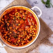 Overhead shot of harissa chickpea stew in a white pot on a woven mat