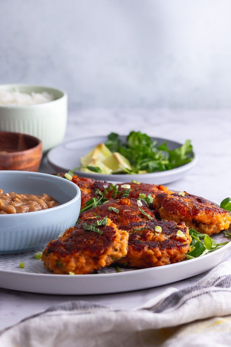 Side on shot of Thai fish cakes on a platter with lime and coriander in the background