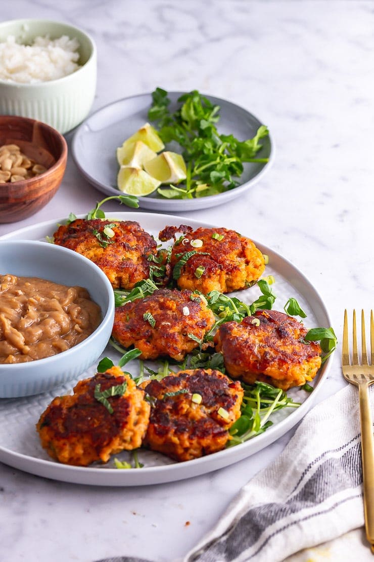 Plate of Thai fish cakes with peanut sauce on a marble background with lime and coriander in the background