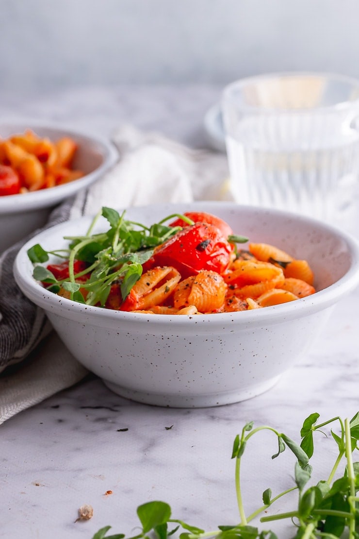 Side shot of tomato pasta in a white bowl on a marble background