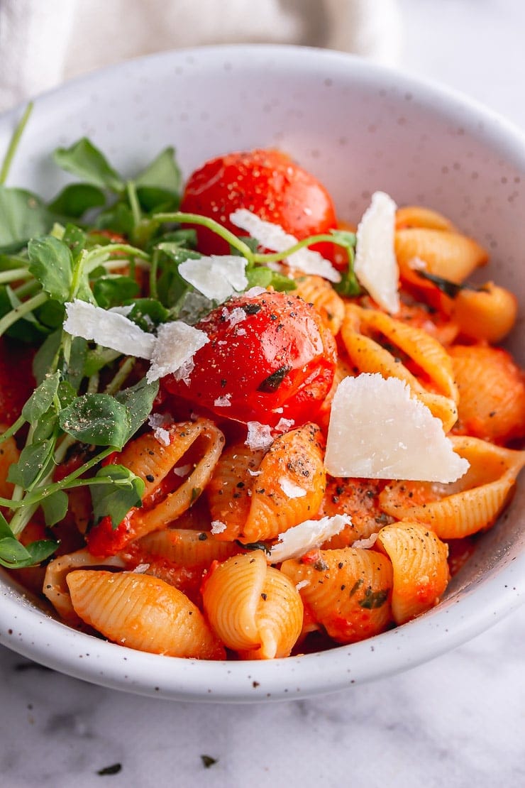 Close up of tomato pasta with greens and parmesan in a white bowl on a marble background