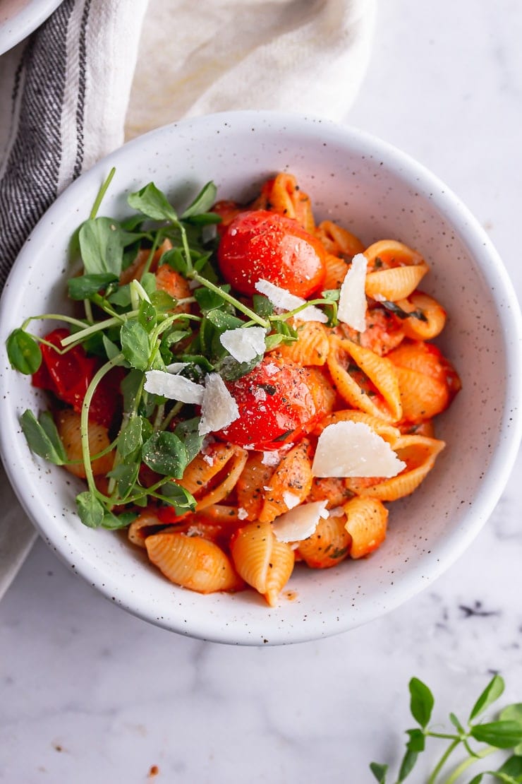 Overhead shot of tomato pasta with greens and parmesan in a white bowl