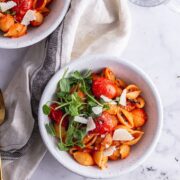 Overhead shot of tomato pasta in white bowls on a marble background