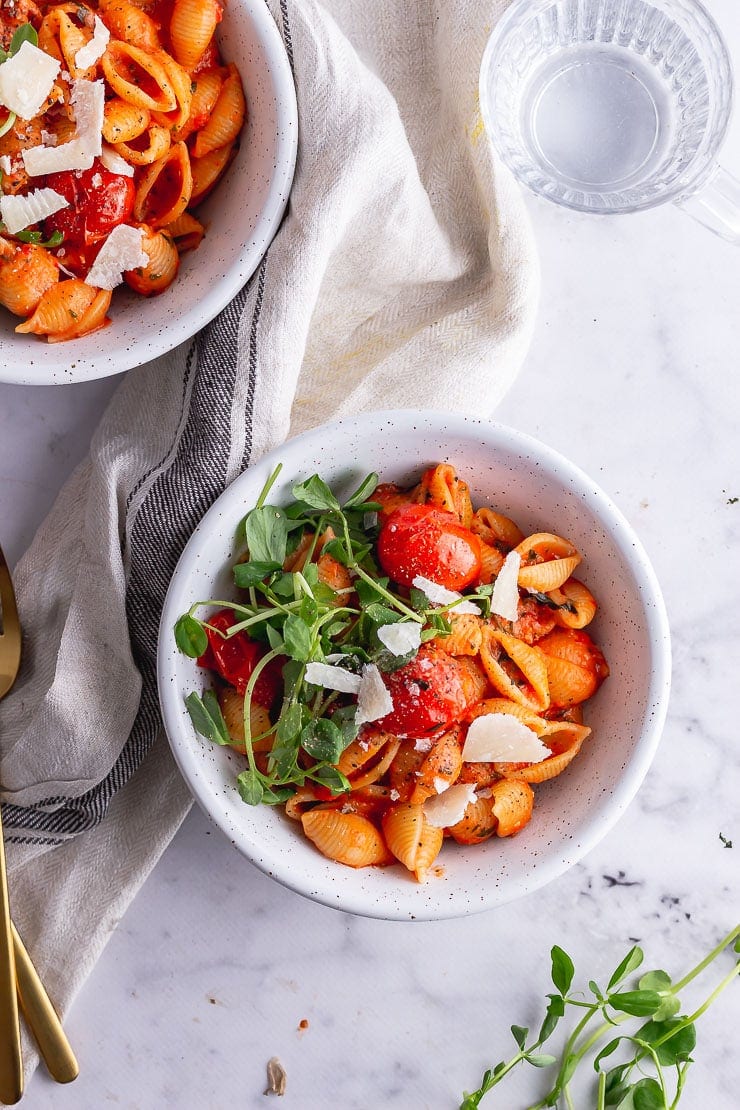 Overhead shot of tomato pasta in white bowls on a marble background