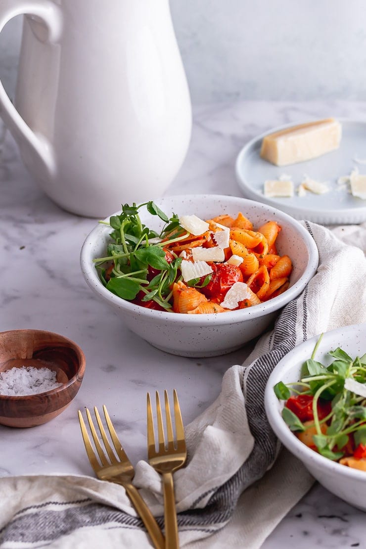 Side on shot of tomato pasta in white bowls with forks and a jug in the background