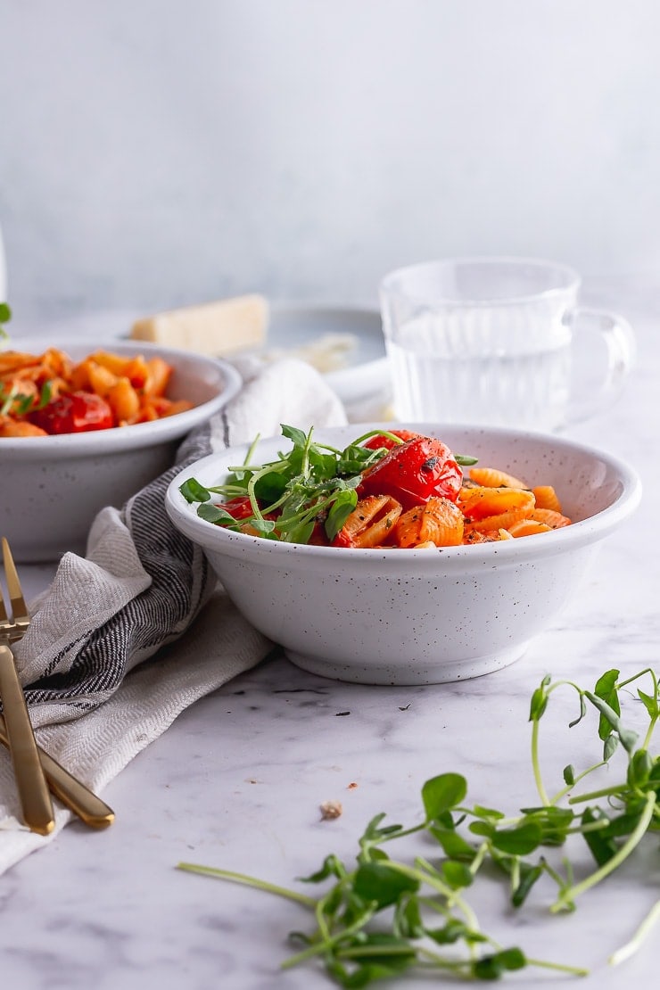 Side on shot of tomato pasta in a white bowl with water and parmesan in the background