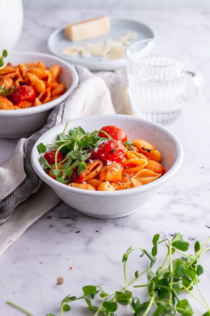 White bowl of tomato pasta with greens in the foreground