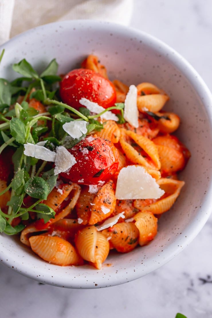 Overhead shot of tomato pasta with greens and parmesan in a white bowl