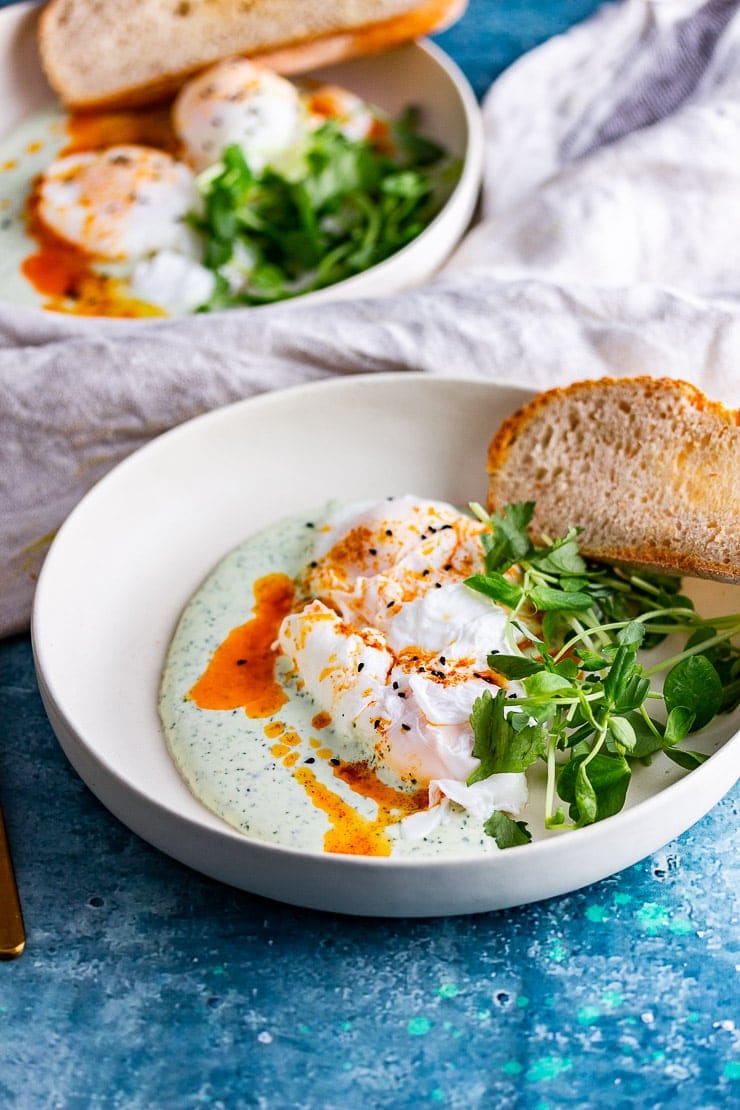 Turkish eggs in a bowl with greens and toast on a blue background