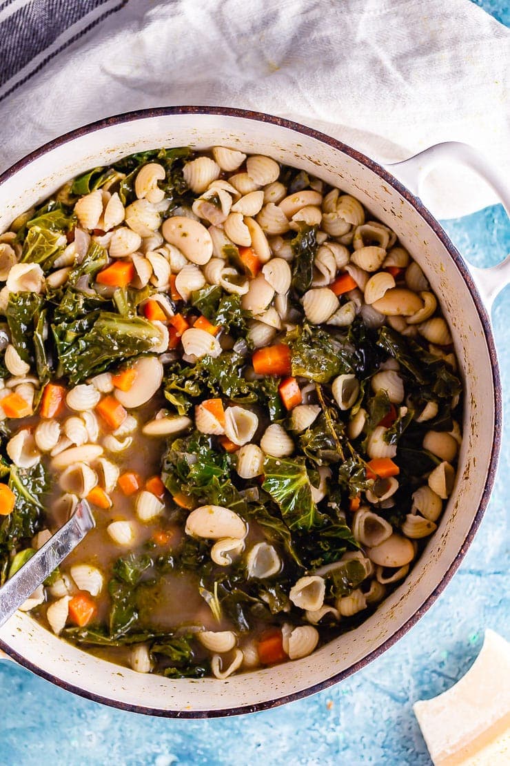 Pot of veggie pesto pasta soup on a blue background