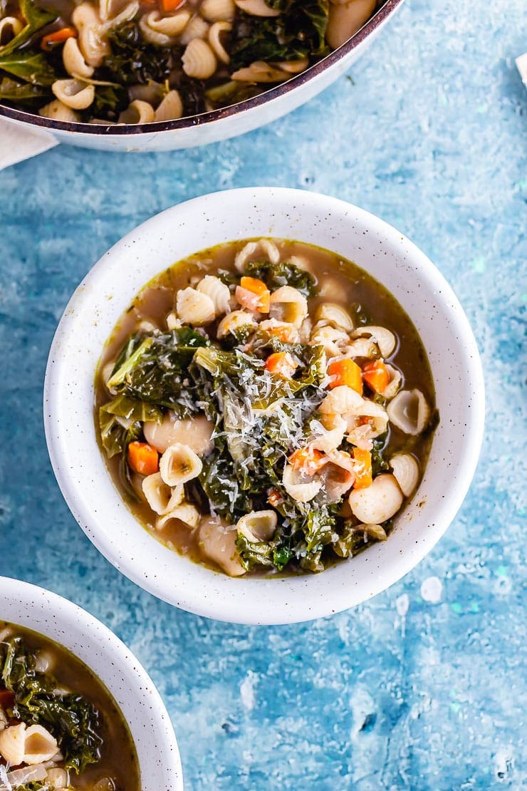 Overhead shot of a white bowl of veggie pesto pasta soup on a blue background