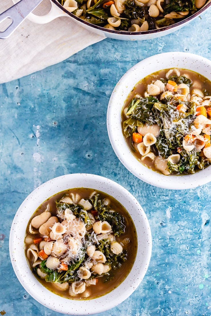 Overhead shot of two bowls of veggie pesto pasta soup on a blue background