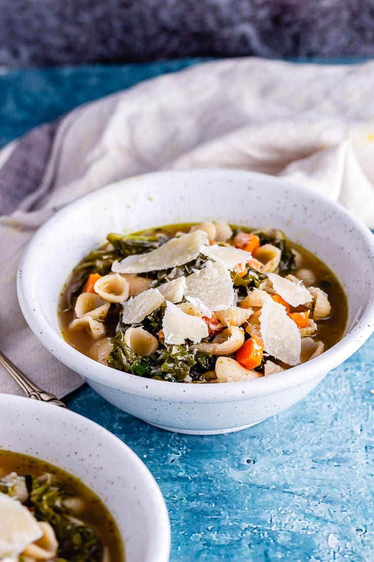 White bowl of veggie pesto pasta soup with a pale cloth