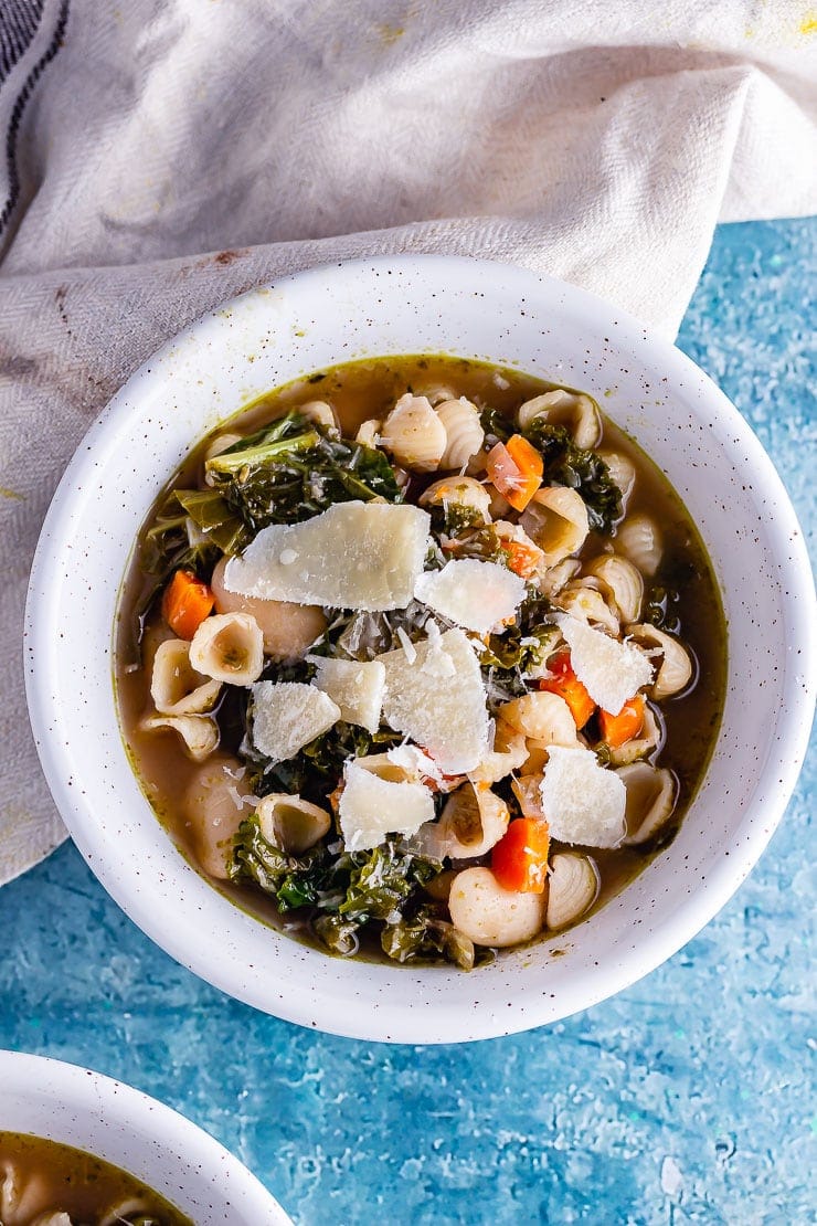 Overhead shot of veggie pesto pasta soup on a blue background with a cloth