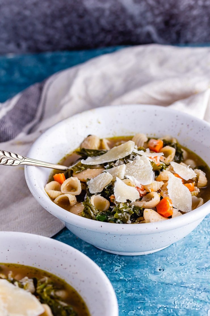 Bowl of veggie pesto pasta soup with a pale cloth and a spoon