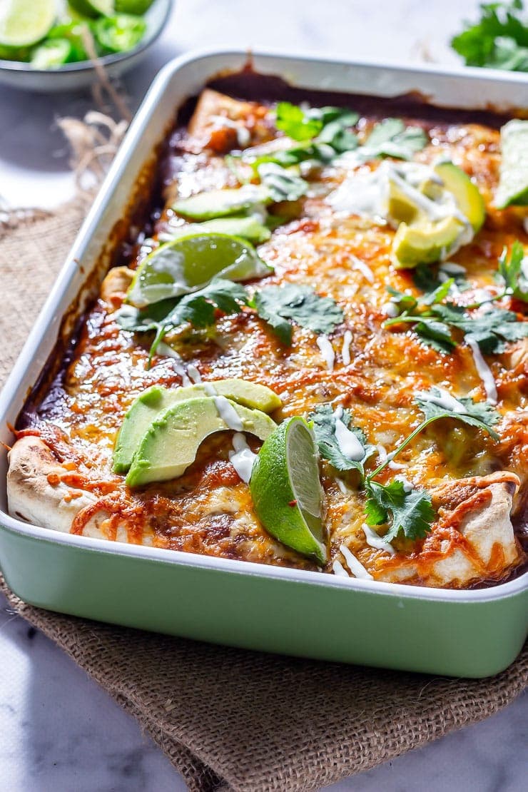 Side on shot of vegetarian enchiladas in a green baking dish on a mat 