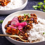 Side on shot of veggie chilli with rice in a white bowl on a dark background