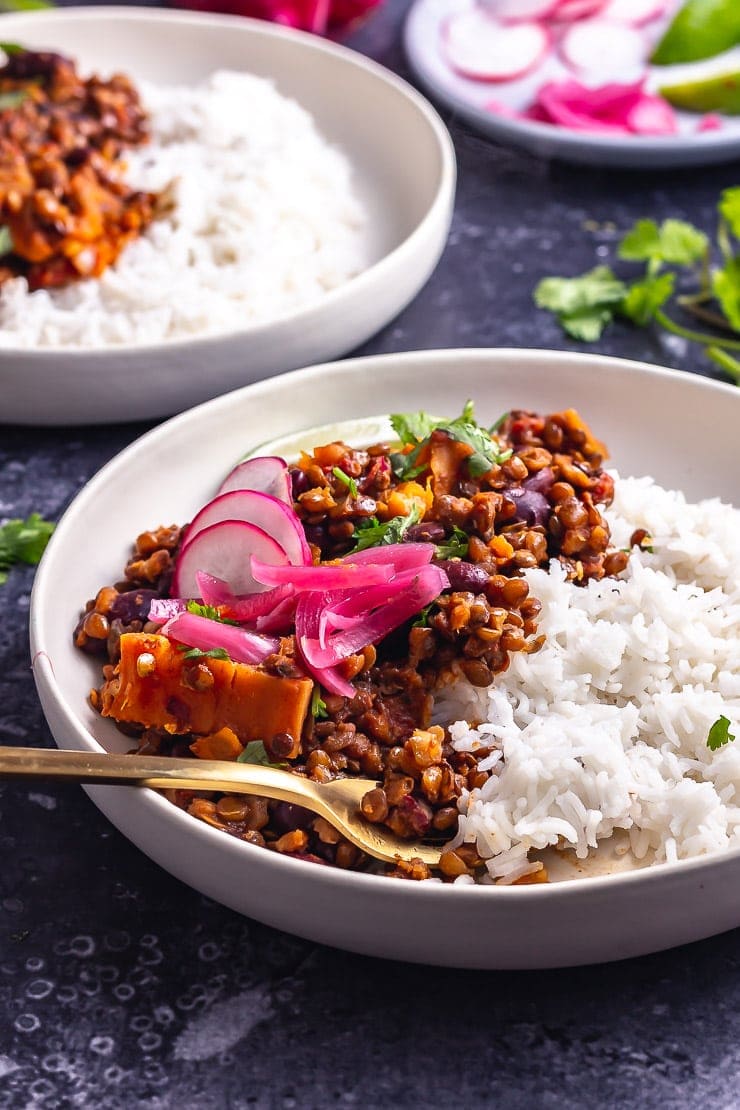 Side on shot of veggie chilli with rice in a white bowl on a dark background