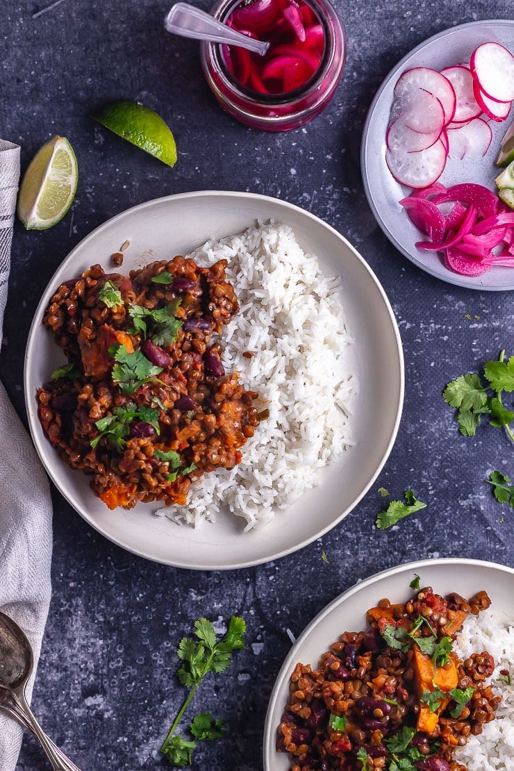 Overhead shot of veggie chilli in white bowls on a dark background with toppings on a plate