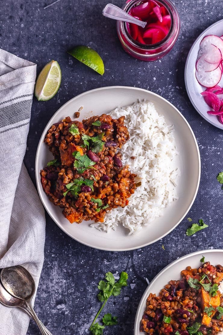 Overhead shot of veggie chilli with rice in a white bowl with toppings and pickled onions