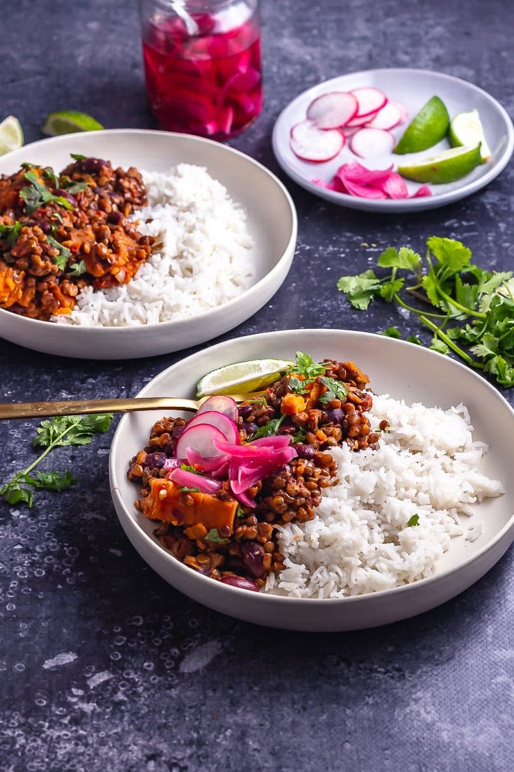 Two bowls of veggie chilli on a dark background with toppings