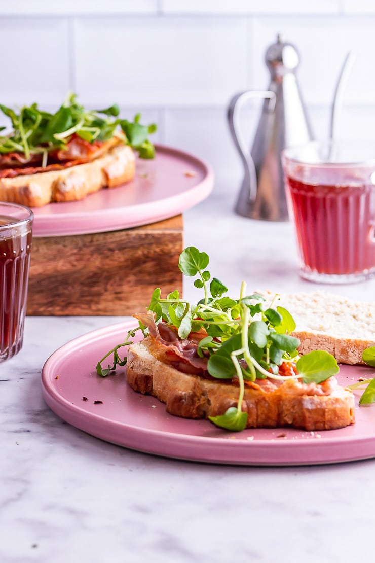 Breakfast sandwich topped with watercress on a pink plate on a marble surface