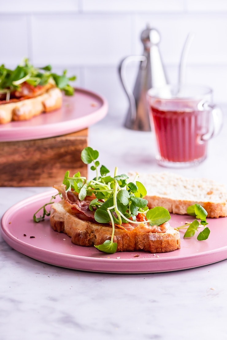 Breakfast sandwich on a pink plate with tea in the background