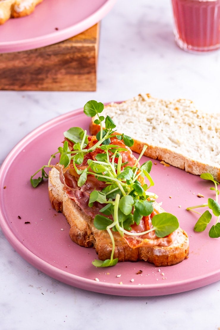 Open breakfast sandwich topped with watercress on a pink plate