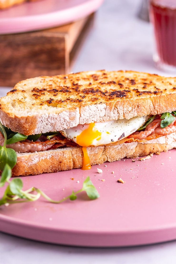 Breakfast sandwich on a pink plate with yolk dripping down the side