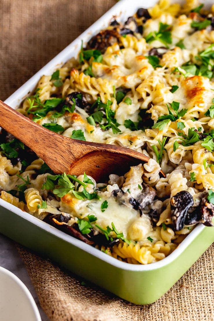 Wooden spoon in creamy mushroom pasta bake on a woven mat