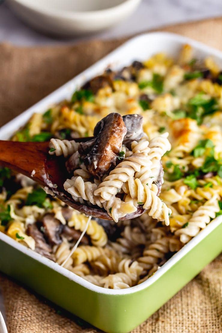 Wooden spoon taking a portion of creamy mushroom pasta bake