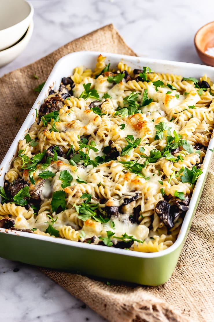 Green baking dish of creamy mushroom pasta bake on a mat