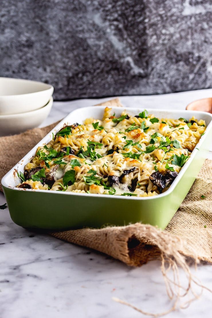 Green baking dish of mushroom pasta bake on a hessian mat over a marble surface